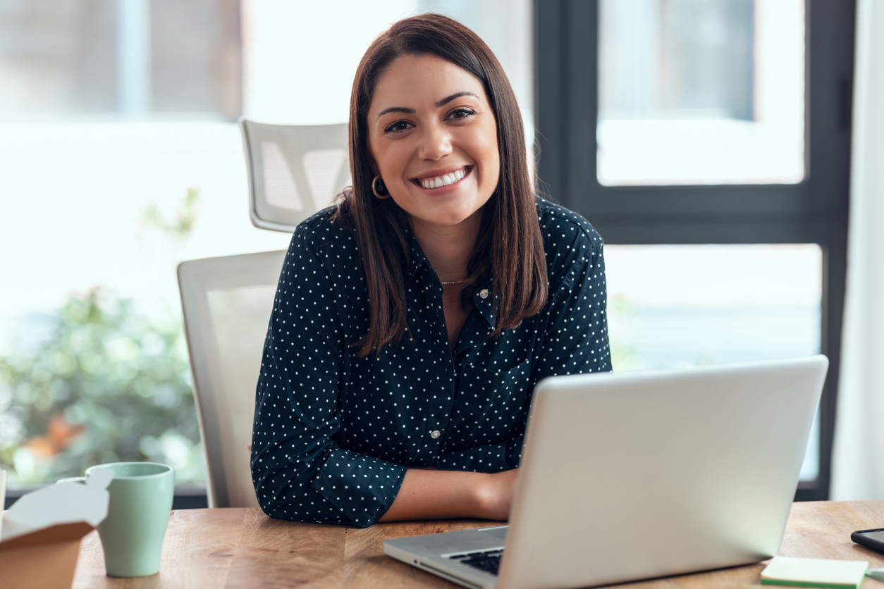 Smiling business woman working with laptop while looking at camera in modern startup office. Sano PS GmbH Team