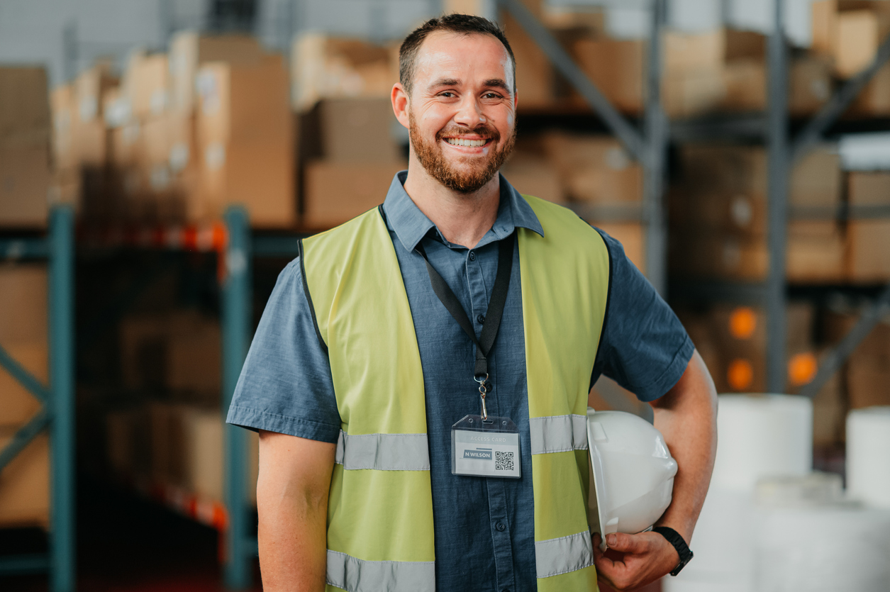 Factory or warehouse worker in a cargo plant happy about the shipping, export and delivery industry. Portrait of a young logistics or supply chain manager smiling about distribution Sano PS GmbH Team
